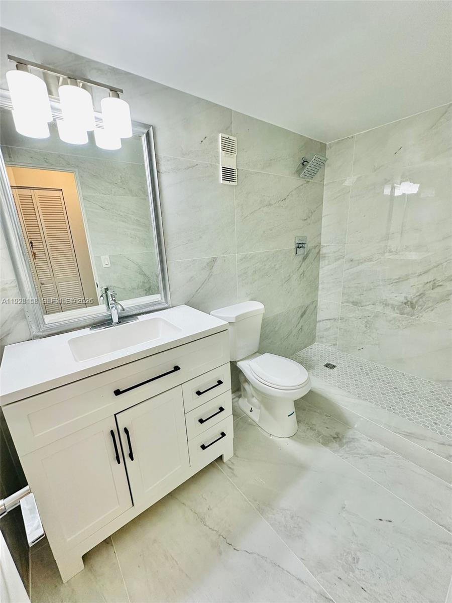 9273 Collins Avenue, Unit 207 Surfside, FL 33154 - Photo 4 of 14 a bathroom with a double vanity sink toilet mirror and shower