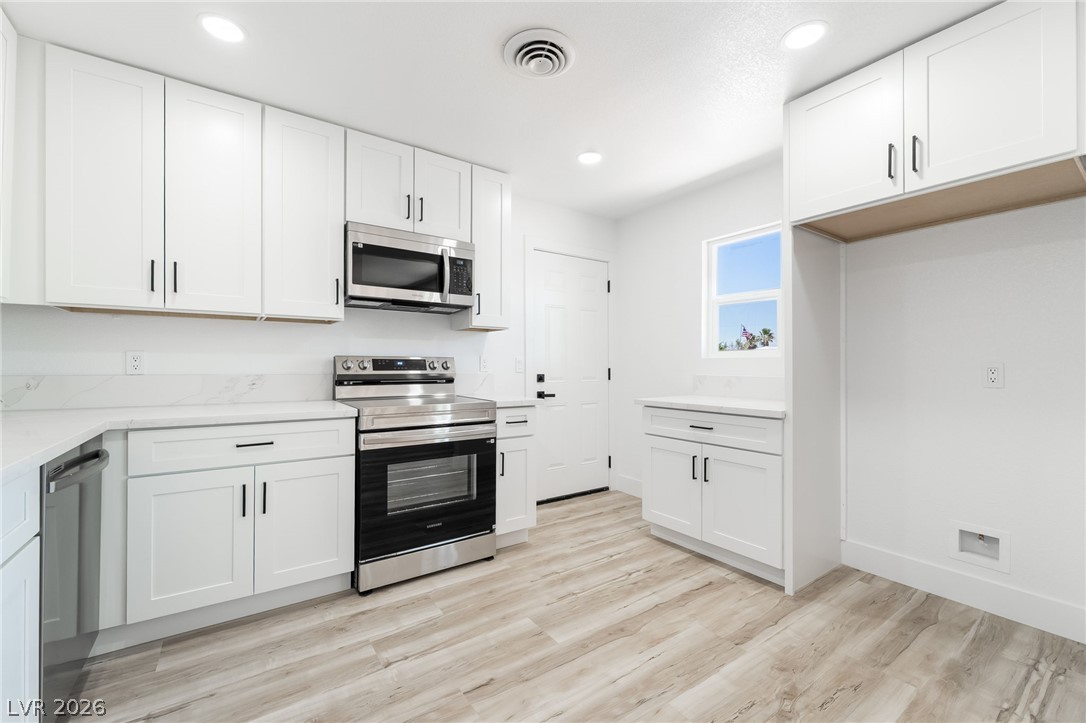 39 Lowery Street Henderson, NV 89015 - Photo 10 of 40 A well-appointed kitchen showcasing contemporary white cabinetry, stainless steel appliances, and wood-look flooring.