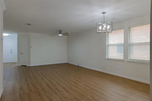 an empty room with wooden floor chandelier and windows