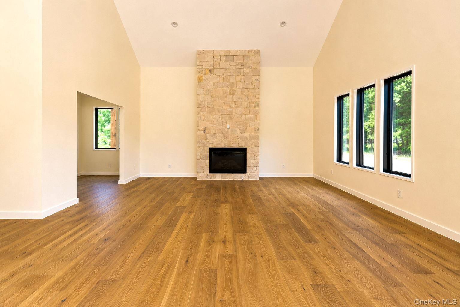 128 St Elmo Road Wallkill, NY 12589 - Photo 13 of 45 Spacious living area featuring a floor-to-ceiling stone fireplace, vaulted ceilings, natural wood-finish flooring, and multiple large windows with black frames. Access to office/den on left off the living room