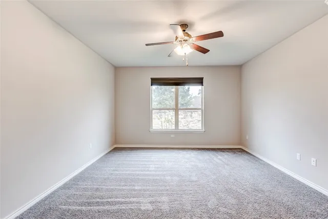 an empty room with chandelier fan and windows