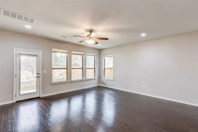 a view of an empty room and kitchen with wooden floor