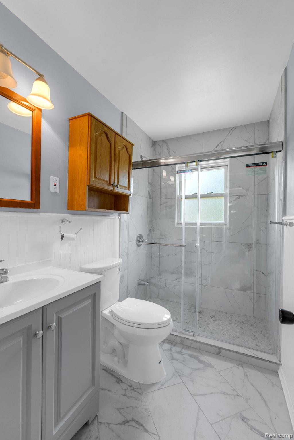 7641 Pelham Road Allen Park, MI 48101 - Photo 13 of 21 Contemporary bathroom featuring a glass-enclosed shower with marble-look tile, a white toilet, and a grey vanity with a white countertop