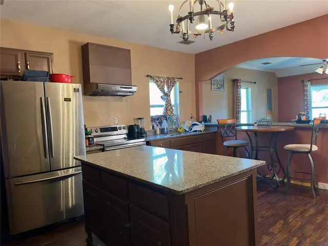 a kitchen with stainless steel appliances granite countertop a refrigerator a sink dishwasher a stove and a dining table with wooden floor