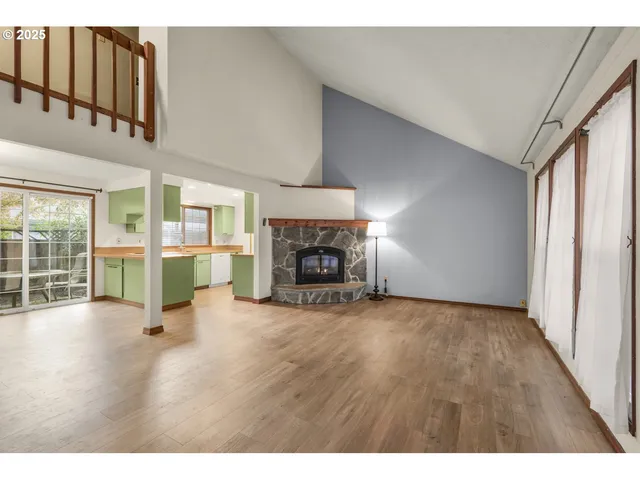 a view of an empty room with wooden floor fireplace and a window