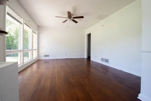an empty room with wooden floor fan and windows
