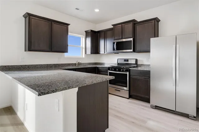 a kitchen with stainless steel appliances granite countertop a stove a sink and a refrigerator with wooden floor