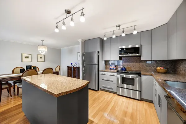 a kitchen with stainless steel appliances kitchen island granite countertop a refrigerator a stove top oven a sink dishwasher and white cabinets with wooden floor