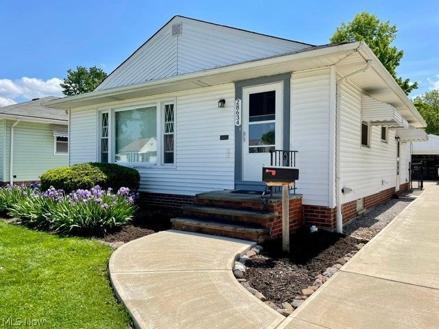 28634 Forest Road Willowick, OH 44095 - Photo 4 of 39 White siding exterior featuring a prominent picture window with decorative side panels, a concrete walkway, brick foundation, and established landscaping with purple blooms