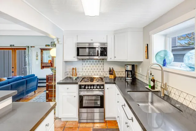 a kitchen with stainless steel appliances granite countertop a stove top oven a sink a dining table and chairs with white cabinets