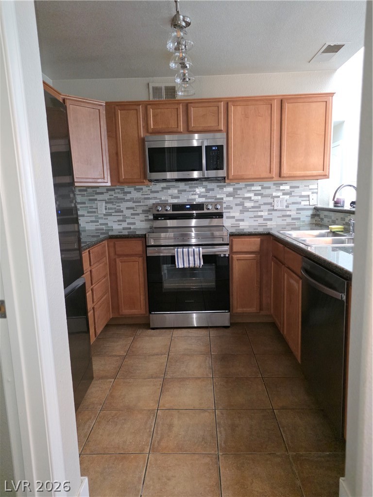 9325 West Desert Inn Road, Unit 239 Las Vegas, NV 89117 - Photo 14 of 29 Kitchen featuring stainless steel appliances, dark stone counters, decorative backsplash, dark tile patterned flooring, and wood finish cabinetry