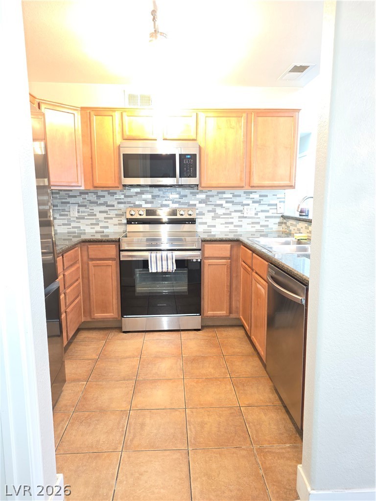 9325 West Desert Inn Road, Unit 239 Las Vegas, NV 89117 - Photo 15 of 29 Kitchen featuring stainless steel appliances, dark stone counters, light tile patterned flooring, and decorative backsplash