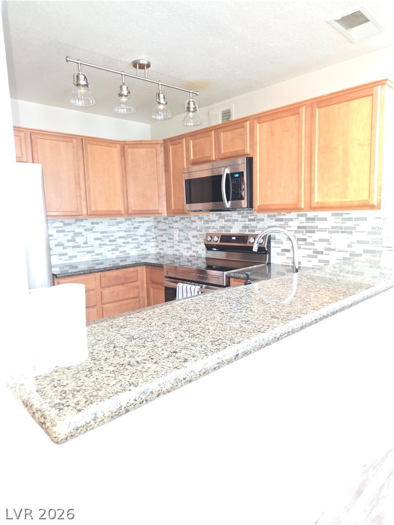 9325 West Desert Inn Road, Unit 239 Las Vegas, NV 89117 - Photo 16 of 29 Kitchen featuring stainless steel appliances, light stone counters, backsplash, a peninsula, and a textured ceiling