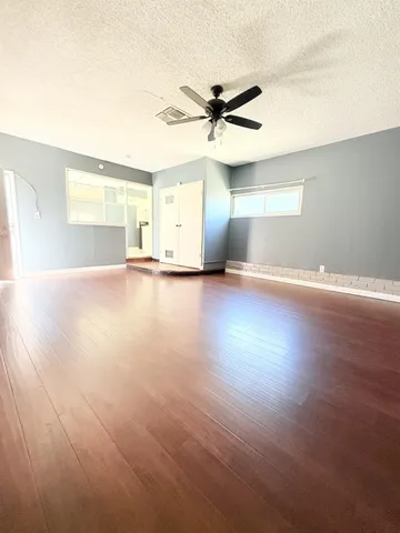 an empty room with wooden floor fan and windows