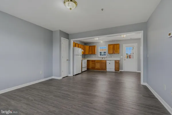 an empty room with wooden floor kitchen view and a fireplace