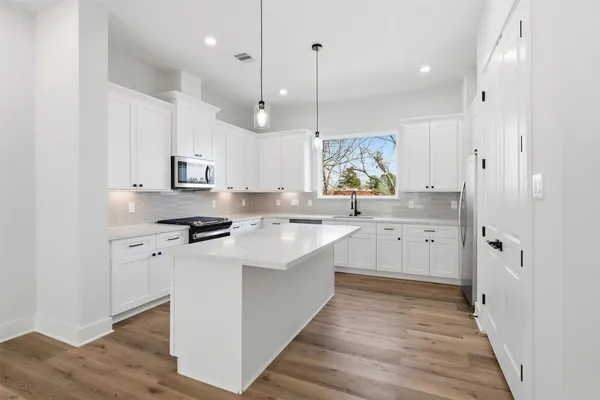 a large kitchen with stainless steel appliances sink a large window and wooden floor