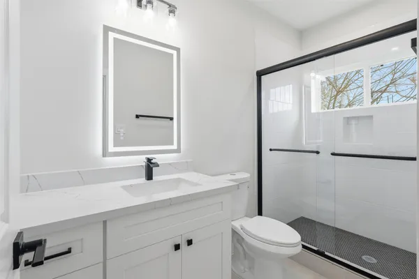 a bathroom with a toilet a sink a mirror a window and vanity