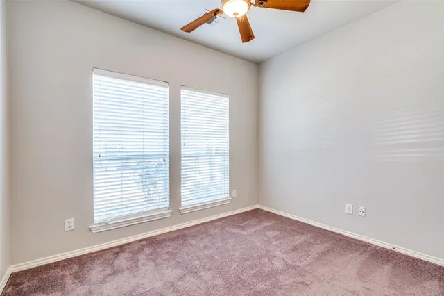 an empty room with chandelier fan and windows