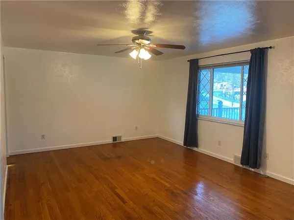 a view of an empty room with wooden floor and a window