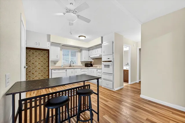 a kitchen with stainless steel appliances kitchen island granite countertop a refrigerator a stove and white cabinets with wooden floor