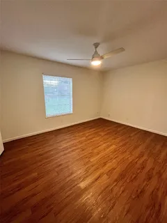 a view of an empty room with wooden floor and a ceiling fan