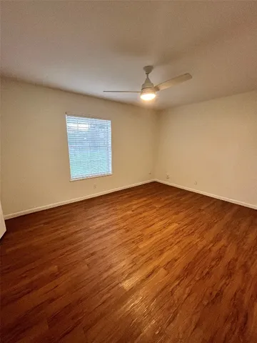 a view of an empty room with wooden floor and a ceiling fan