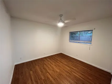a view of an empty room with wooden floor and a ceiling fan