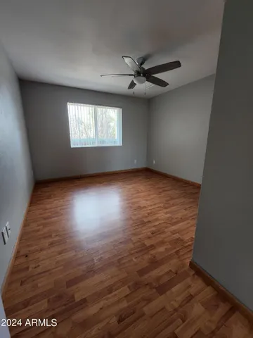 an empty room with wooden floor chandelier fan and windows