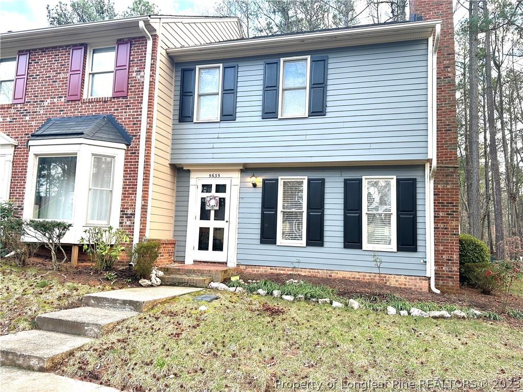 front view of a brick house with a large window and potted plants