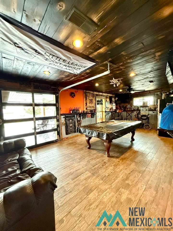 5404 Sioux Road Carlsbad, NM 88220 - Photo 39 of 100 Spacious recreational area featuring wood-finish flooring, a full-view garage door, a prominent bar area, and exposed wood plank ceiling