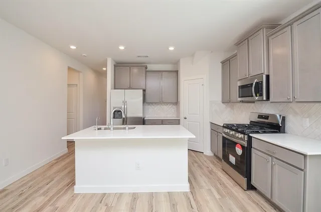 a kitchen with stainless steel appliances granite countertop a sink a stove top oven a refrigerator with white cabinets and wooden floor