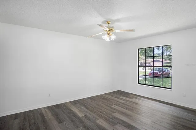 an empty room with wooden floor chandelier fan and windows