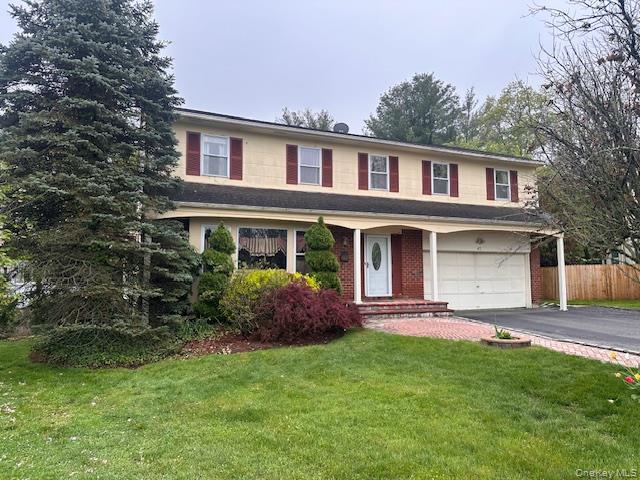 Traditional-style house with an attached garage, driveway, fence, and a front yard
