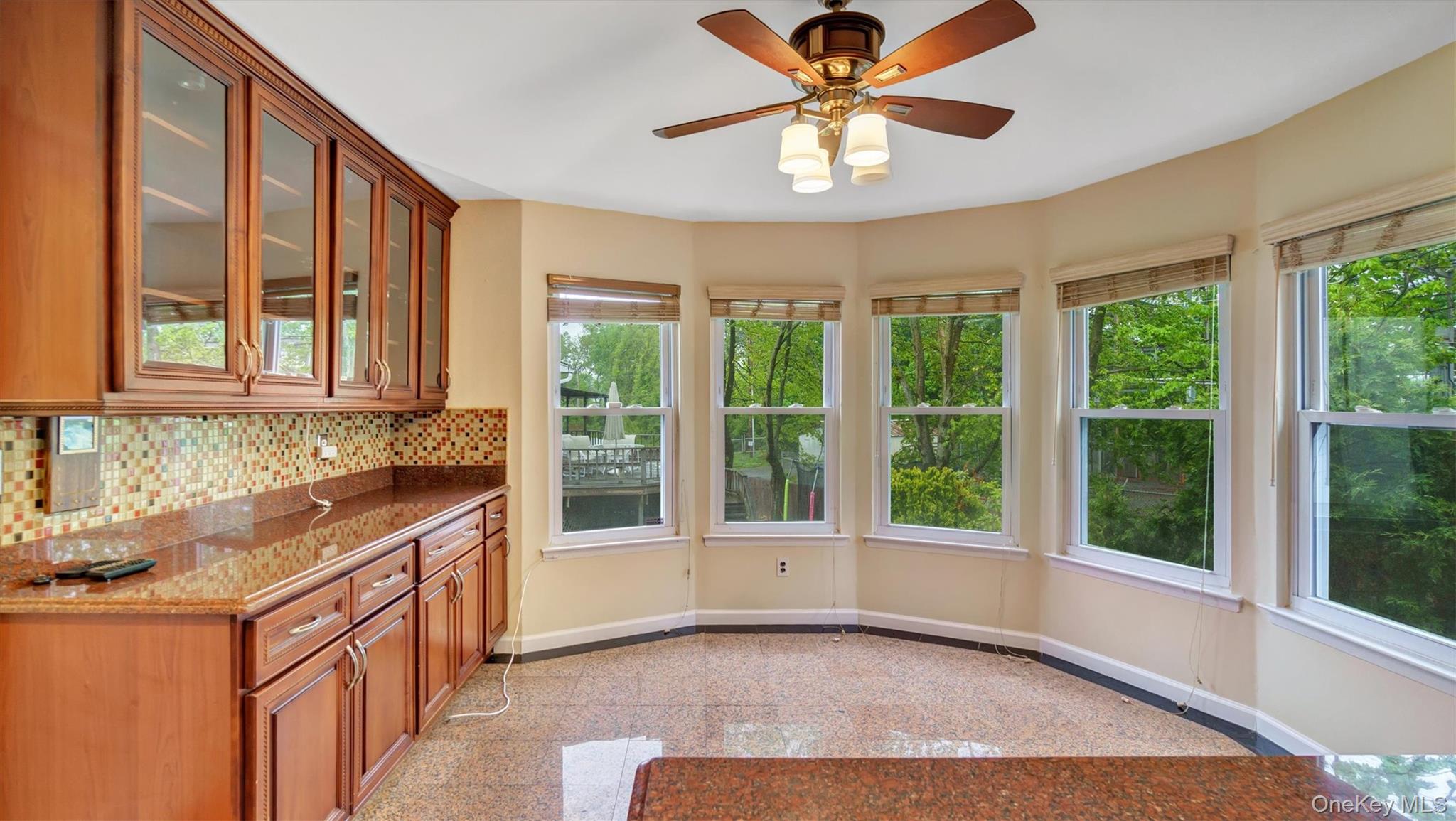 47 Carriage Road Roslyn, NY 11576 - Photo 11 of 31 Kitchen featuring brown cabinetry, backsplash, granite finish floor, glass insert cabinets, and baseboards