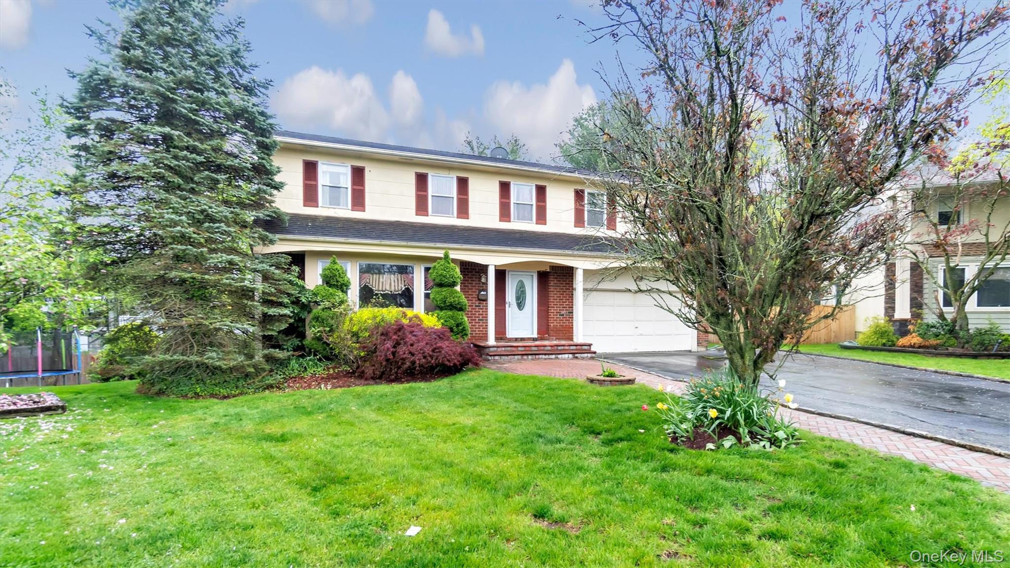 47 Carriage Road Roslyn, NY 11576 - Photo 2 of 31 Traditional-style house featuring brick siding, a garage, a trampoline, a front yard, and aphalt driveway