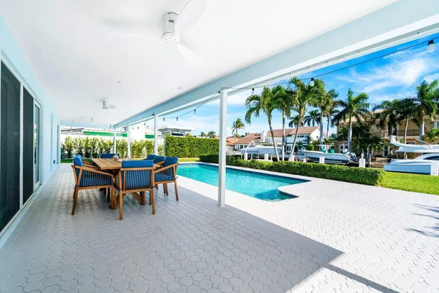 a view of swimming pool that has lawn chairs with plants and palm trees