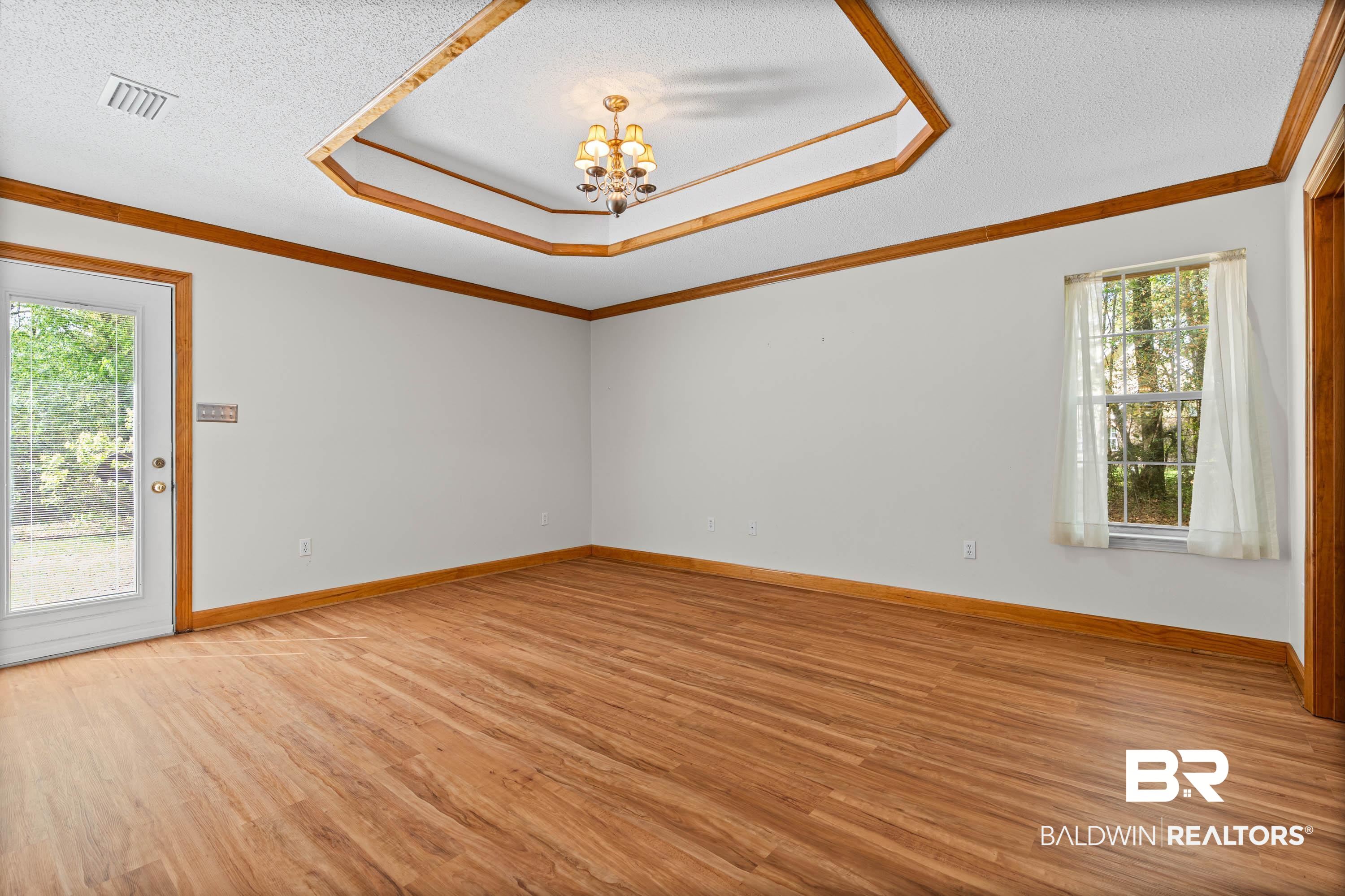 10140 Lakeview Road Bay Minette, AL 36507 - Photo 14 of 35 Empty room featuring a textured ceiling, a chandelier, light wood-style floors, crown molding, and a raised ceiling