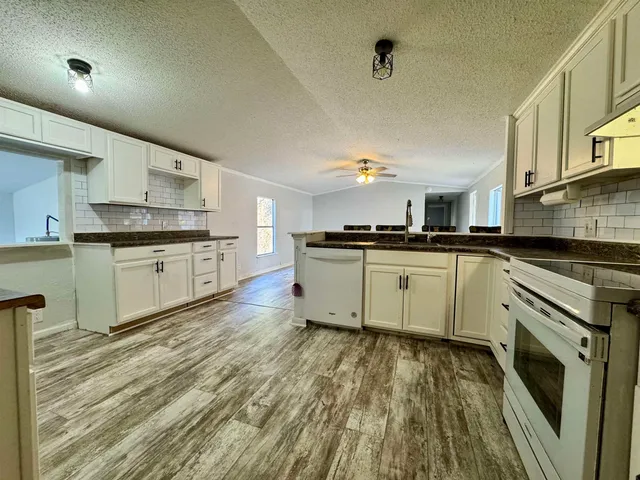 a kitchen with stainless steel appliances granite countertop a stove top oven a sink dishwasher and white cabinets with wooden floor