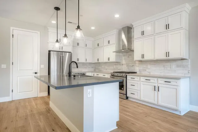 a kitchen with stainless steel appliances granite countertop a sink a stove a refrigerator and white cabinets with wooden floor