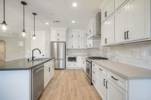 a kitchen with stainless steel appliances granite countertop a stove a sink dishwasher a refrigerator and white cabinets with wooden floor