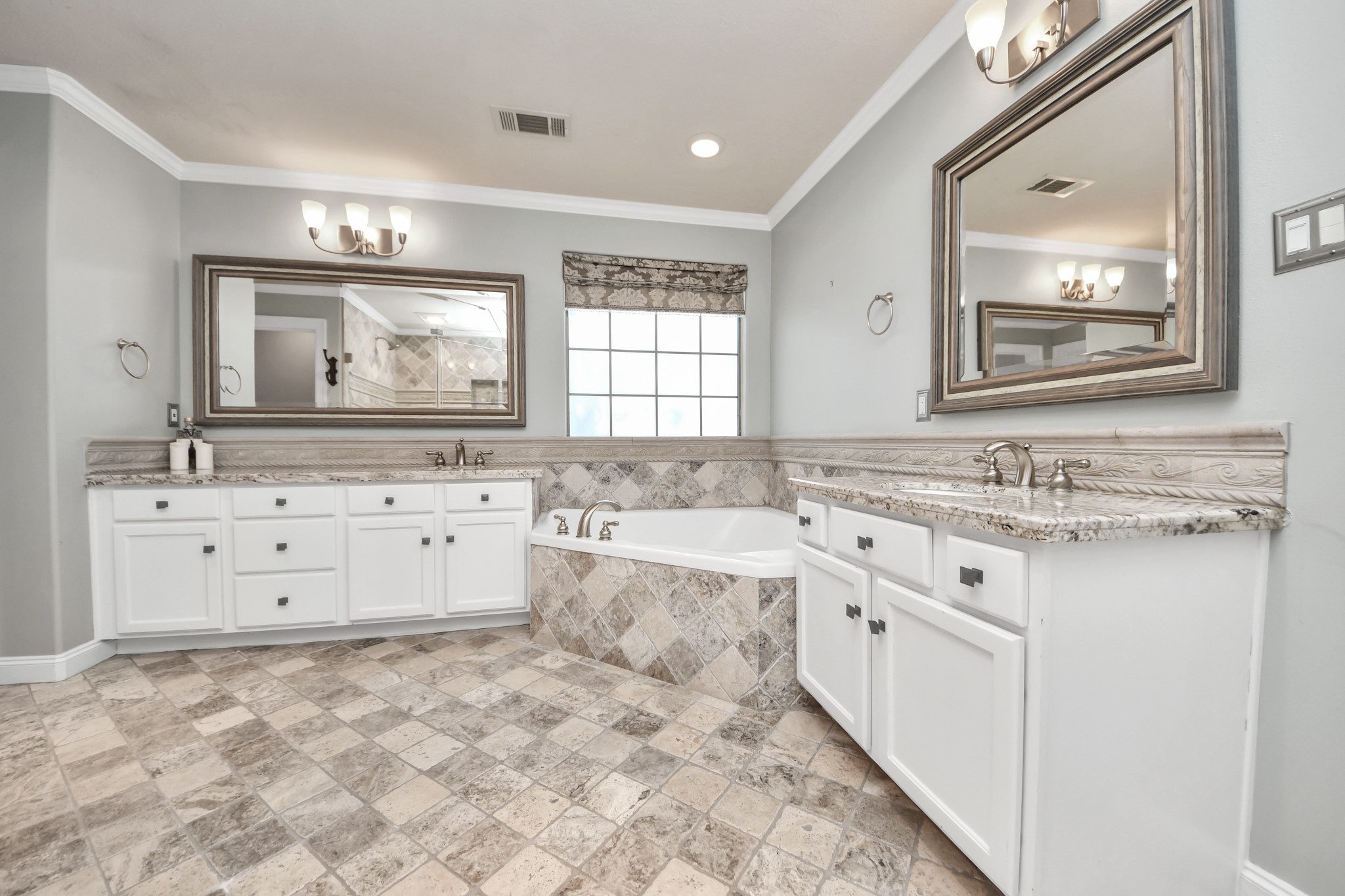 710 Jackson Hill Street Houston, TX 77007 - Photo 24 of 31 This spacious bathroom features dual vanities with granite countertops, a central soaking tub, elegant tile flooring, and large mirrors, creating a luxurious and functional space.