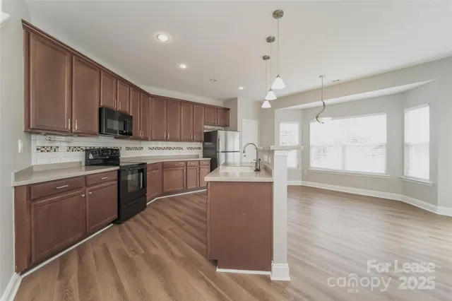 a kitchen with stainless steel appliances granite countertop a stove top oven a sink dishwasher and a refrigerator with wooden floor