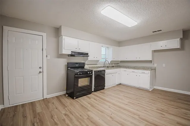 a kitchen with granite countertop a refrigerator oven a sink and white cabinets