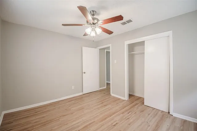 an empty room with wooden floor closet and ceiling fan