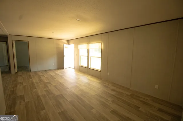 an empty room with wooden floor and windows with curtains