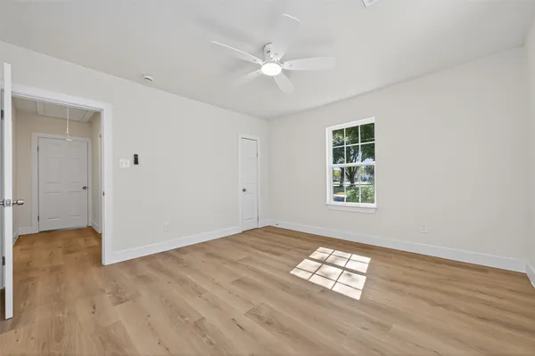 an empty room with wooden floor chandelier fan and windows