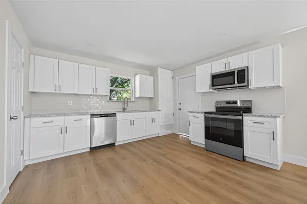 a kitchen with granite countertop a stove top oven a sink dishwasher and a refrigerator with wooden floor