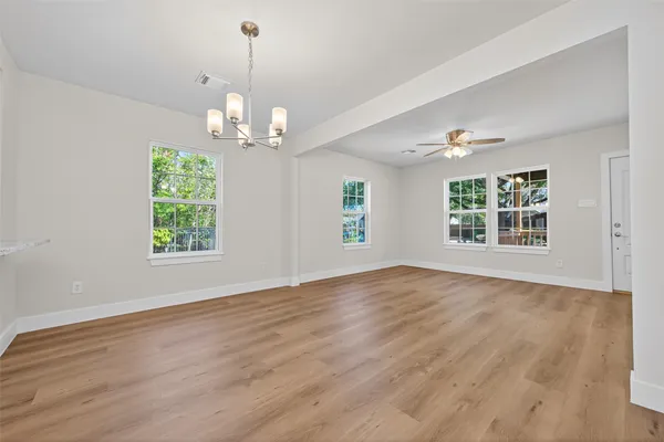 an empty room with wooden floor chandelier and windows
