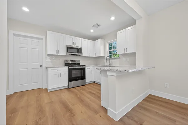 a kitchen with stainless steel appliances granite countertop a stove top oven a sink and white cabinets