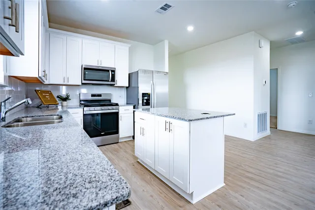 a kitchen with stainless steel appliances granite countertop a refrigerator a sink a stove a microwave and white cabinets